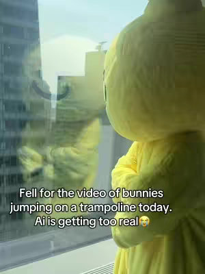 The image shows a person in a yellow bunny costume, looking out a window. The reflection in the window shows a blurred version of the bunny costume, and the city outside. Text overlays the bottom of the image.