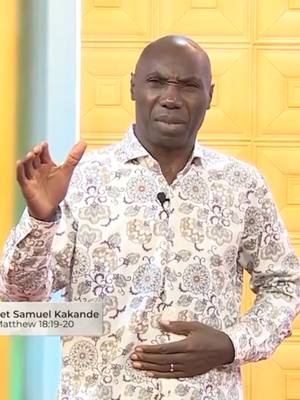 A dark-skinned man wearing a patterned shirt stands in a yellow-toned background, gesturing with one hand and touching his stomach with the other. Text overlays are present.