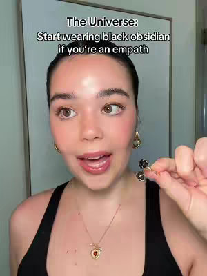 The cover image shows a young woman in front of a plain white wall. She's wearing a black tank top and gold jewelry, and holding out a black obsidian ring. The text overlay says, "The Universe: Start wearing black obsidian if you're an empath."