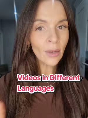 A woman with long brown hair looks directly at the camera, with text overlayed on her face. The text is in a pink box with a white outline and includes the words "Videos in Different Languages".