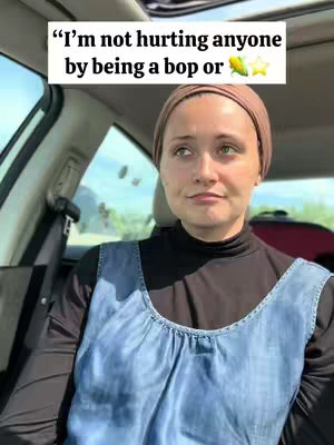 A woman with a head covering is seated inside a car, looking pensively off-camera. Text overlaid on the image reads: 'I'm not hurting anyone by being a bop or 🌽⭐'. The background shows the interior of a car, with a partially visible seat and window.