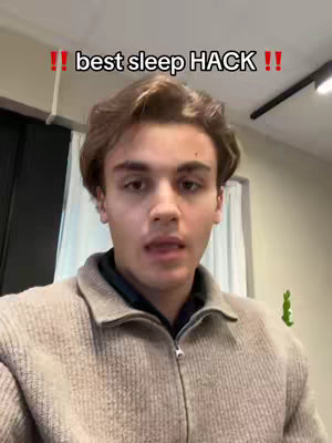A young man is centered in the frame, looking towards the camera with a neutral expression. He's wearing a beige zip-up jacket over a dark collared shirt. Above his head, in bold red text, reads "!! best sleep HACK !!". The background is a simple interior scene with white walls, a dark doorway to the left, and a bright light fixture. The composition is straightforward, focusing on the man's face and the text overlay.
