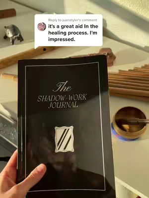 The cover image shows a close-up of a book with a black cover and a silver border. In the center, there is a silver framed design. A hand is holding the book, and in the background are various objects including a small statue and a wooden wind chime.