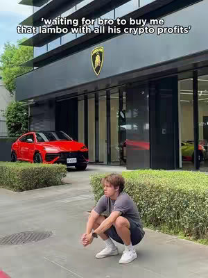 A young man in casual wear crouches in front of a modern building and a red sports car, showcasing a luxury car dealership; above, overlaid text humorously states a request.