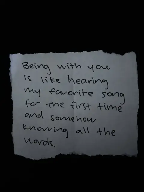 A close-up shot of a piece of torn paper on a black background. Handwritten text is on the paper. The edges of the paper are uneven.