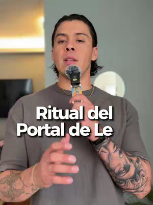 A man with dark hair and tattoos is centered in the frame, holding a small microphone. The background is a neutral gray. Text overlays the image.