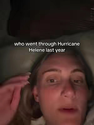 A selfie-style shot taken from the point of view of a person lying in bed, with soft lighting and a dark background. The main subject is a blonde woman with fair skin and a neutral expression, visible from the chest up. The words "who went through Hurricane Helene last year" are in white text across the top.