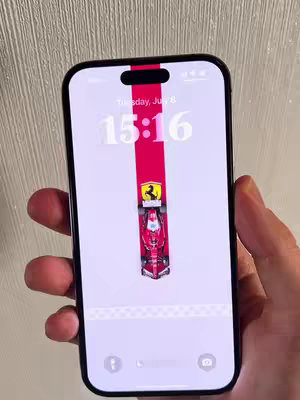 A hand holding a mobile phone showing a custom wallpaper of a red F1 race car with the Ferrari logo. The lock screen displays the time and date.
