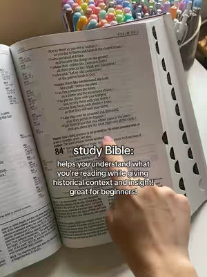 An overhead shot features an open Bible with a hand pointing to a passage. The text overlay reads 'study Bible: helps you understand what you're reading while giving historical context and insight! great for beginners!' Pens are visible in the background.