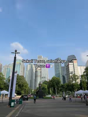 An outdoor scene features a cityscape with numerous tall buildings under a bright blue sky. In the foreground, a road leads to a statue in the distance. Text overlays are added at the top of the image.