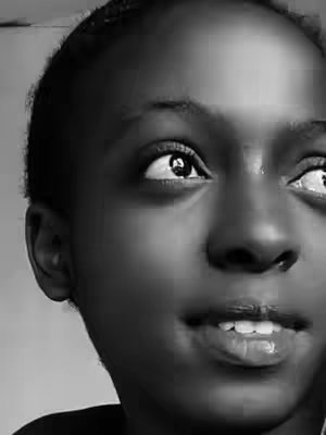 A black and white close-up shot of a person's face, focusing on their eyes and mouth. The person appears to be looking upward and slightly to the right, with a hint of a smile. The lighting is soft, highlighting the facial features.