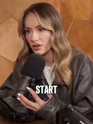 A medium shot of a woman with long blonde hair, a white top, and a black leather jacket holding a microphone. The word 'START' is overlaid in a white outlined font.