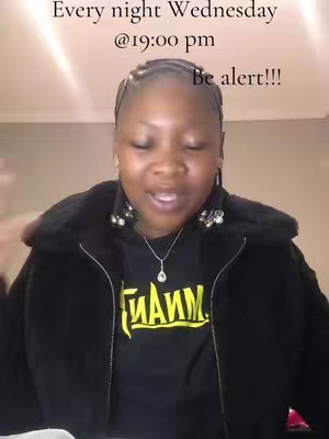 A woman in a black jacket is centered, looking towards the viewer with a small smile. Text overlays at the top with a time and day for alerts. A black t-shirt is visible beneath the open jacket, with some yellow text. The lighting is fairly neutral, and the background is a simple wall.