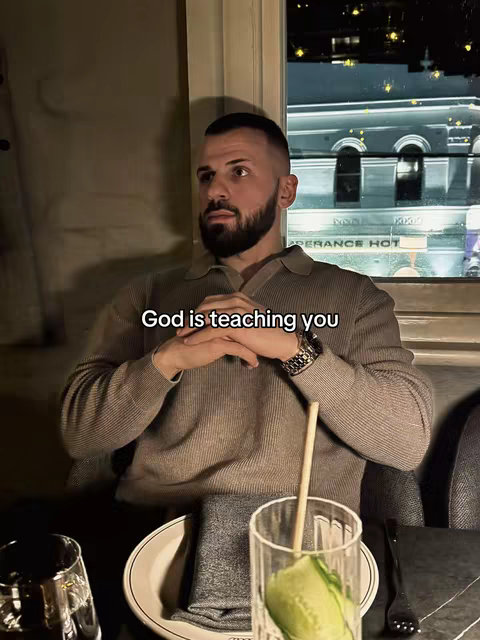 A man with a beard is seated at a table in a restaurant or bar setting. The man looks up and to the left with a contemplative expression. The text overlay adds a layer of a religious message.