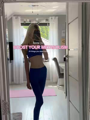 The cover image is a selfie taken in a large, ornate mirror. A young woman with blonde hair is in the center, wearing a blue sports bra and matching leggings. She is holding her phone up, partially obscuring her face. Text overlays read: "how to BOOST YOUR METABOLISM (4 things you need to do)." The background includes a window with curtains, a pink yoga mat on the floor, and glimpses of a tidy interior. The overall impression is health and wellness-focused, with a clean and bright aesthetic.
