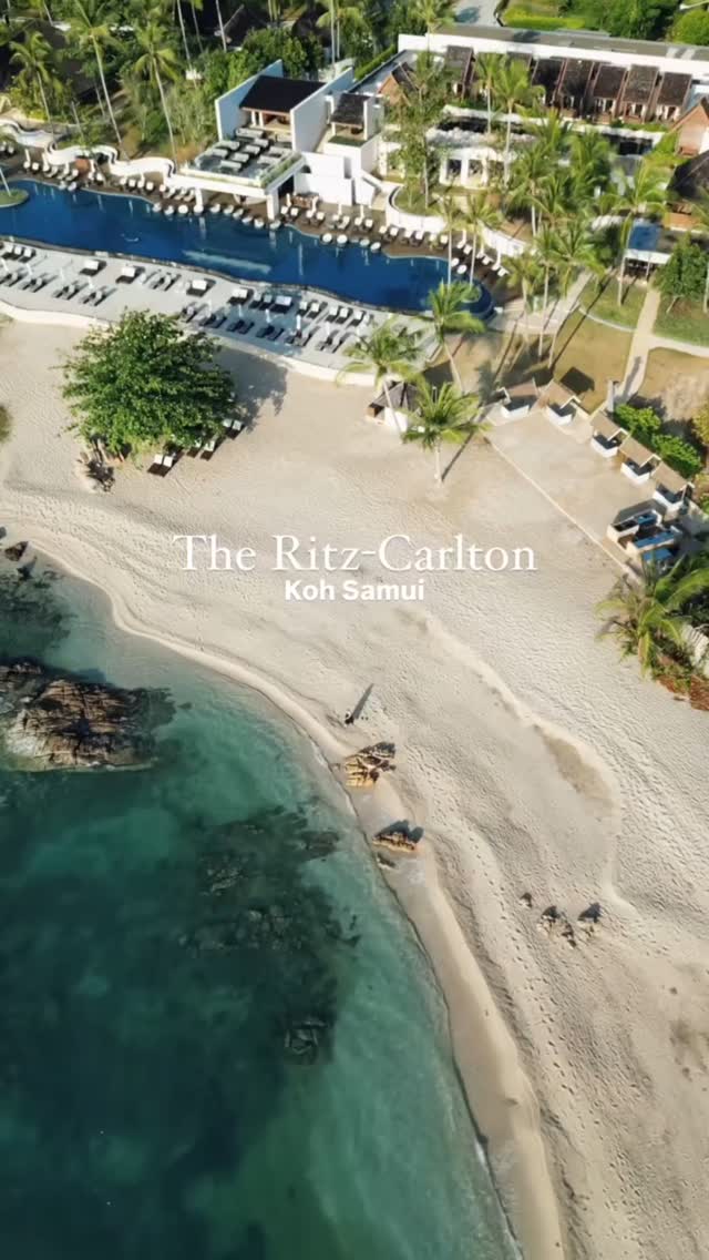 An aerial view showcases the Ritz-Carlton Koh Samui. The image highlights a pristine white sand beach leading to turquoise waters, with coconut trees lining the shore. A hotel complex featuring a large pool and resort buildings is seen at the top. The overall composition is inviting, with natural light highlighting the resort's features.