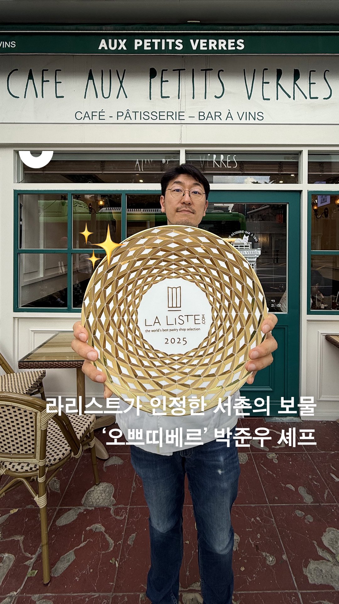 A man is holding a circular golden award with a patterned design. The background includes a cafe with a green and white facade, and the image includes overlaid text in Korean.