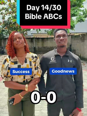The image shows two people standing side by side, a woman on the left and a man on the right, against an out-of-focus background. At the top, there is a text overlay in a colored rectangle. The woman is wearing a patterned blouse, gold bracelets, and has reddish-brown hair. She is holding a phone. The man wears a black jacket, and the word Goodnews is on a label below. A score of 0-0 is at the bottom of the image.