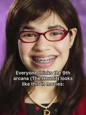 A selfie-style shot of a young woman smiling directly at the camera. She wears red-framed glasses and a pearl necklace with a 'D' pendant. The background is a solid purple color.