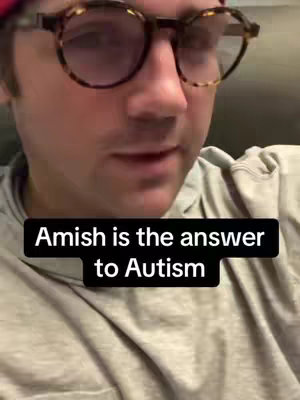 The cover image is a close-up of a person, likely the creator, viewed from the chest up. They are wearing large, round eyeglasses with a tortoiseshell pattern, and a light-colored hoodie. The text overlay, against a solid black background, reads 'Amish is the answer to Autism'. The background appears to be a neutral indoor setting, and the lighting is soft. The person is looking towards the viewer, implying direct address.