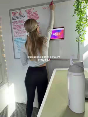A woman with blonde hair is writing on a whiteboard with various notes. She has her back to the camera. She is wearing a white long-sleeved shirt and black leggings. There is a digital timer on a tablet in the background, with the timer showing "00:24". A white water bottle is visible on the right side. "Obsession's gonna be talent every time" appears in text over the bottom.