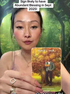 The cover image features a woman holding a tarot card in front of a green, forest-like background. The woman has fair skin, dark hair pulled back, and is wearing jewelry. The tarot card depicts a man standing in front of a tree. The overall composition is a close-up shot, focusing on the woman and the card.