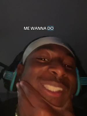 A selfie-style video cover image showing a young man with dark skin, smiling widely. Above him, a text overlay reads "ME WANNA DO". He is wearing headphones around his neck and a white headband. The background is dark.