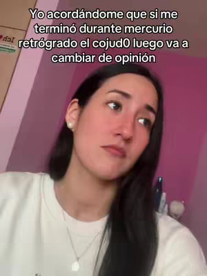 A woman with long dark hair and fair skin is looking slightly off-camera. She is wearing a white top and a silver necklace with a pendant. The background is a soft light pink color. The text overlay reads: "Yo acordándome que si me termino durante mercurio retrógrado el cojudo luego va a cambiar de opinión".