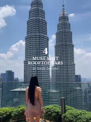 A woman stands on a rooftop overlooking the skyline of Kuala Lumpur, with the Petronas Towers prominently in the background. Text overlayed on the image reads "4 MUST VISIT ROOFTOP BARS in Kuala Lumpur". The woman is seen from the back with long, dark hair. The composition is symmetrical with the towers as the central element and the woman placed to the foreground.