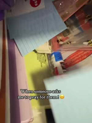 The image is a medium close-up, slightly top-down view, of a cluttered space, likely a desk or organizer. Visible objects include various sheets of paper, some blue lined and others yellow, with text, and a red round sticker in the background. A blue and white tube or bottle is present. The lighting is dim, giving a sense of a room. The text overlay is in white.