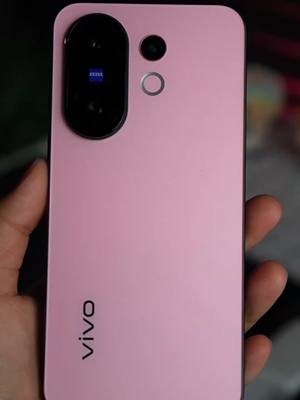 The image showcases a close-up view of a pink smartphone held in a hand. The phone features a camera module on the top left. The phone is pink, has the vivo logo at the bottom.