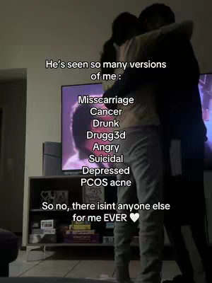 A couple is embracing in a dimly lit room, with the woman in the foreground and a man wrapped around her. Text overlays on the image list various challenges the woman has faced, such as miscarriage, cancer, and depression.