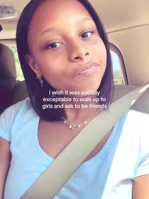 A close-up shot of a young woman in a car. She’s looking at the camera with a slight smile, wearing a light blue t-shirt and a delicate necklace. A seatbelt is visible across her body, and text overlaying the image conveys a message about social interactions. The background subtly shows car interiors and an outdoor setting.
