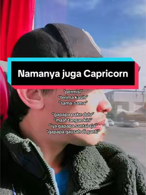 A selfie-style video with a man wearing a black cap, captured from the chest up. A text overlay in a black box with white text reads 'Namanya juga Capricorn.' Below this, a series of statements are displayed in white text, likely quotes, with the background showing a blurred cityscape and sky.