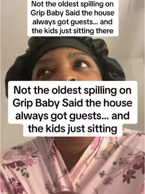 A selfie-style video cover featuring a Black woman wearing a black head covering and a pink floral robe. The image has two white rectangular text boxes overlaying the image with text about a situation involving a person known as Grip Baby and the kids being present. The woman looks up and to the left, with a slightly confused expression. The background is a plain white wall.