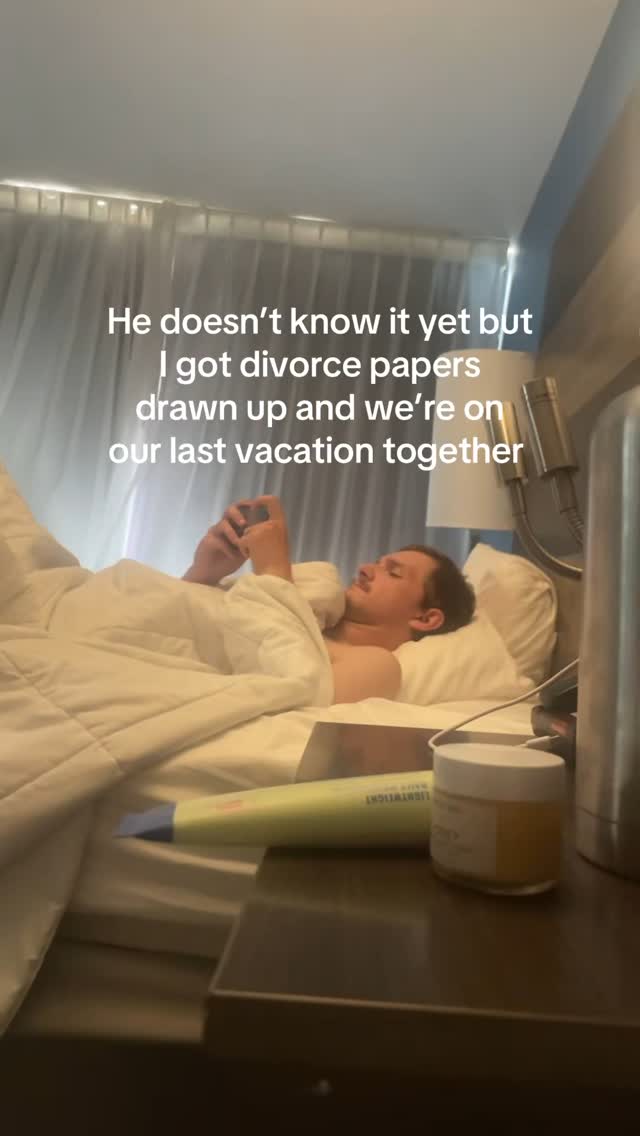 A man is lying in bed, looking at his phone. Above him is text that reads: 'He doesn't know it yet but I got divorce papers drawn up and we're on our last vacation together.' The scene is lit with soft lighting. The man is under a white duvet.