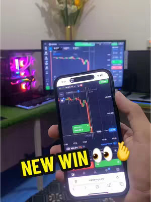 A person's hand holds a smartphone displaying a stock trading app with a green and red candlestick chart. The background features a computer, monitor, and a vase with flowers. A text overlay says 'NEW WIN'.