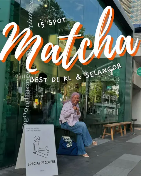 A woman is sitting on a stool in front of a glass storefront, smiling towards the camera. The storefront has a sign that says "SPECIALTY COFFEE."  Large text overlays across the top of the image read "15 SPOT Matcha BEST DI KL & SELANGOR". The image is brightly lit with natural light giving off a sunny vibe. There is a bench and a sign on the street near the window. 
