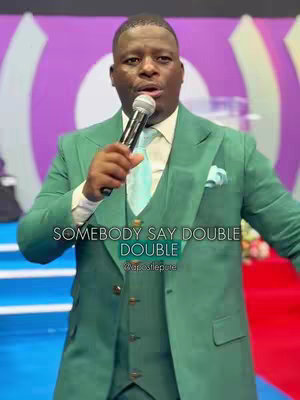 A man in a green suit is holding a microphone, with a background that appears to be a stage or auditorium, with text overlaid.