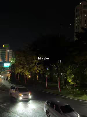 The image shows a nighttime cityscape with a road curving through the center. Cars with headlights on travel down the road. Streetlights and buildings are visible in the background. Text is overlaid on the image.