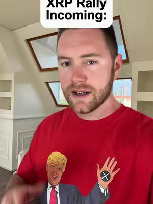 A man in a red shirt is speaking to the camera. The shirt features a cartoon of a man making a hand gesture with a hand displaying the XRP cryptocurrency logo. Above the man's head is a white rectangle with the text 'XRP Rally Incoming:'. The background includes neutral wall and architectural features.