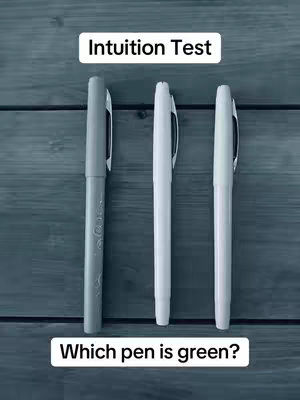 The image shows three pens against a wood-grain background. The pens, each a different shade of grey, are positioned vertically. Text at the top indicates the image is an "Intuition Test", and text at the bottom asks "Which pen is green?"
