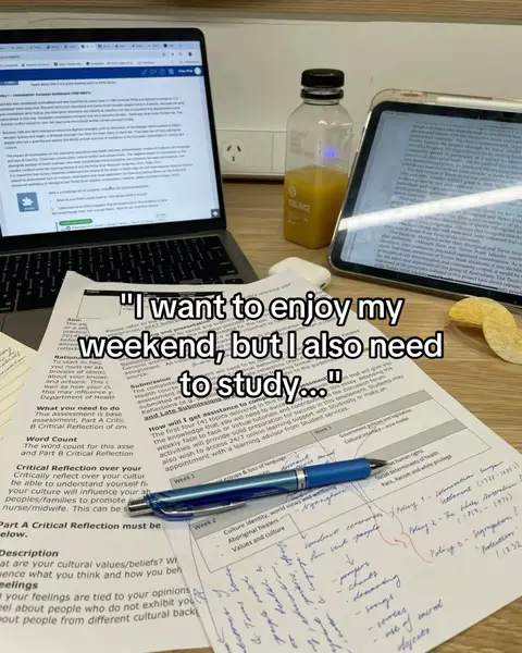 The image shows a laptop, an iPad, and some scattered papers on a wooden desk. A bottle of orange juice sits between the laptop and iPad. The image has a warm, slightly desaturated color palette.