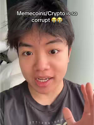 A young man with short black hair looks directly at the camera, speaking with a concerned expression. Above him, overlaid text reads "Memecoins/Crypto is so corrupt" with emoji eyes. The background is blurred, suggesting an indoor setting.