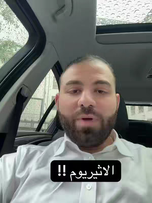 A man wearing a white shirt looks toward the camera while sitting in the driver's seat of a car. A black text box with the word الاثيريوم is placed at the bottom of the image.