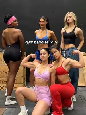 A group of five women pose in a gym setting. Most are wearing activewear, with some flexing their biceps. Text overlayed reads 'gym baddies >>>'.