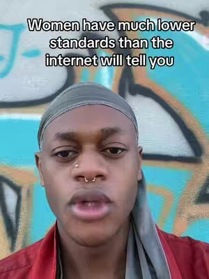 A close-up of a Black person looking at the camera. They are wearing a gray head wrap and red shirt. The background is a blurred image of colorful graffiti.