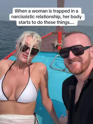 A selfie-style shot taken outdoors on what appears to be a boat. A woman and a man are in the frame, both wearing sunglasses and smiling. The woman is in the foreground and is wearing a white bikini top. Behind them is blue water and a portion of a wooden boat. There is text overlaid at the top of the image.