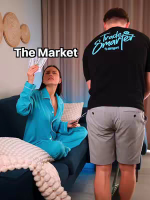 The image shows a woman sitting on a sofa holding cash and looking up with an expression of astonishment. The background includes decorations and another person standing nearby. Text overlaying the image reads, "The Market."