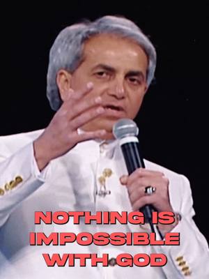 The image features a man speaking into a microphone with a text overlay. The man is fair-skinned with short, graying hair. He wears a white suit and holds a microphone in his left hand. The text overlay, in a red font, reads "NOTHING IS IMPOSSIBLE WITH GOD". The background appears to be a dark, potentially stage-like setting.